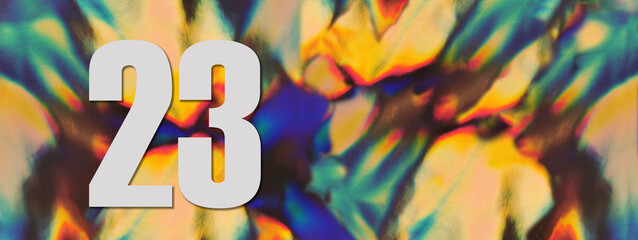 Wide banner. Number 23 twenty three on the blurry iridescent holographic foil background. Colorful reflective folia. Greeting card. Copy space. Flat lay.