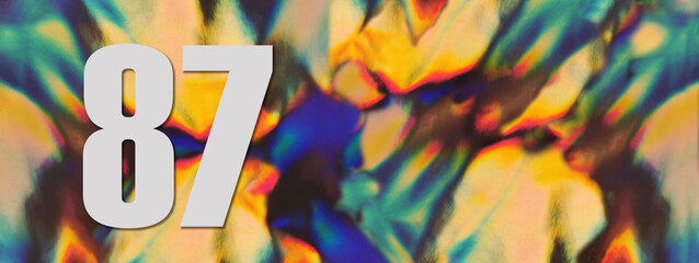 Wide banner. Number 87 eighty seven on the blurry iridescent holographic foil background. Colorful reflective folia. Greeting card. Copy space. Flat lay.