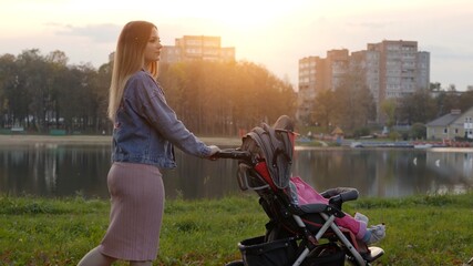 Fototapeta na wymiar A young mother with a stroller walks in the autumn evening.