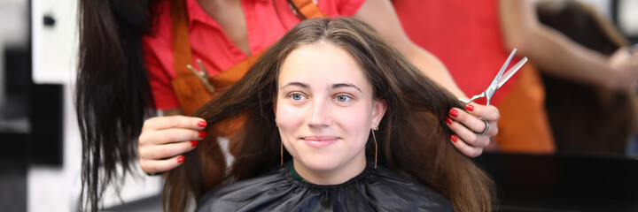 Smiling female master hairdresser holds hair of client and scissors in hands. Hairdresser training and courses concept