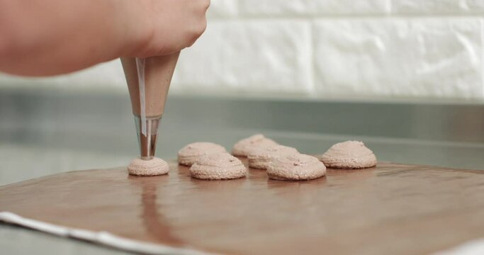 Chef making base for preparation macaron dessert. Close-up of extruding brawn creme from piping bag on metal tray for baking base of macaron dessert.
