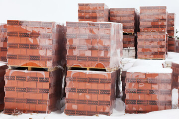 Preparing for the construction of a house, a break from construction for the winter. Packages of red bricks lie outside under the snow