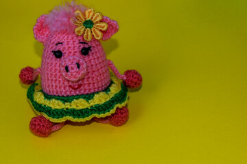 Fototapeta na wymiar Pink, crocheted pig in a green skirt on a yellow background. Knitted toy pig.
