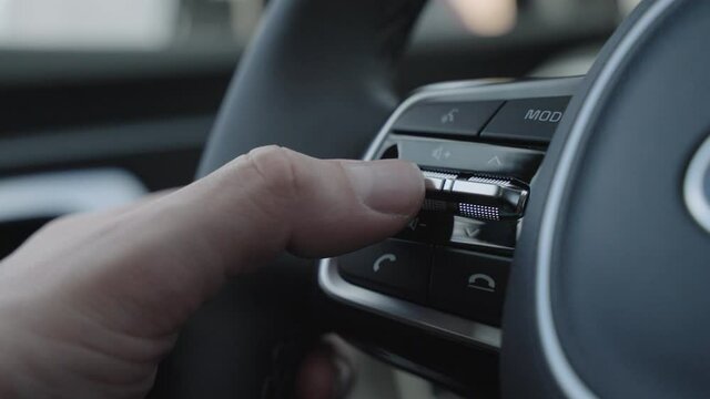 Close up of finger pressing the audio control buttons to increase or decrease the volume on the steering wheel when driving. Steering wheel audio volume adjust