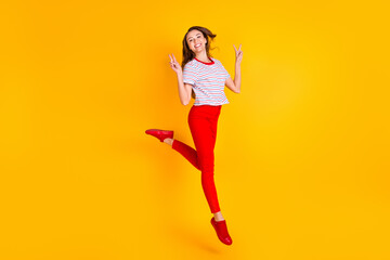 Photo of charming funny lady jump show two v-signs wear striped shirt red pants shoes isolated yellow color background