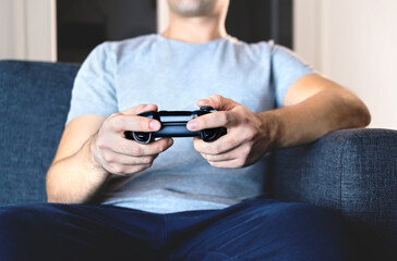 Video game controller in hand for console gaming. Gamer guy playing tv videogame with control gamepad or joystick while sitting home couch. Fun weekend online streaming. Happy man and player.