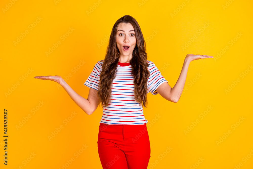 Poster portrait of attractive amazed cheerful girl holding on two palms copy space new novelty offer isolat