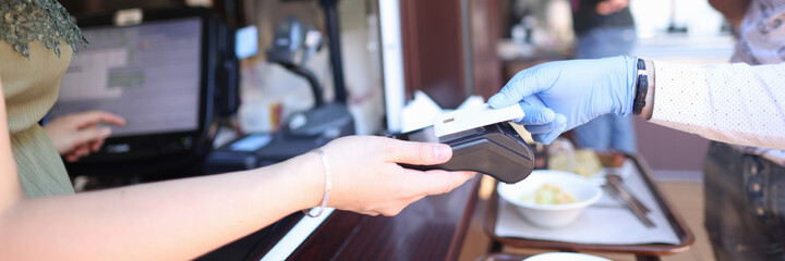 Hand in protective glove holds a bank card cashier holds out terminal for payment. Payment by bank cards in a pandemic concept
