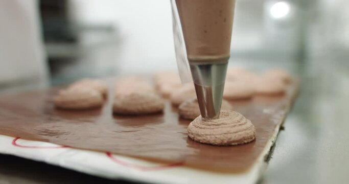 Chef making base for preparation macaron dessert. Close-up of extruding brawn creme from piping bag on metal tray for baking base of macaron dessert.
