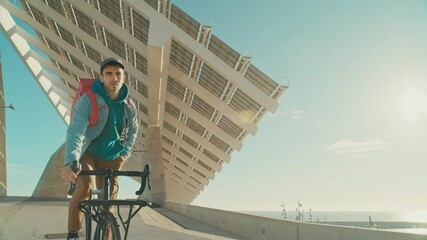 Handsome stylish young man on bike ride to work or university on commuter bicycle. Student or office worker commute on sunny morning in modern urban city space. Look at smartphone when cycling