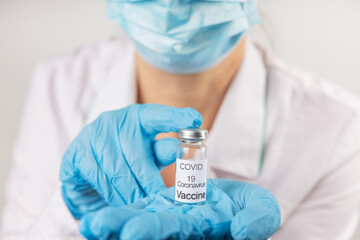 Vial with COVID-19 vaccine against coronavirus infection in the hand of a doctor in a nitrile glove on a white background. Close-up. Fight against coronavirus concept