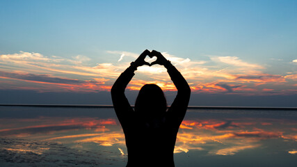 Frau formt mit den Händen ein Herz vor dem Sonnenuntergang