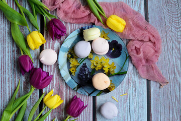Spring composition in a rustic style. Lilac and yellow tulips and a plate with multi-colored marshmallows on a wooden background. Top view