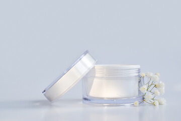 Layout of an empty jar and flowers for cream, mask, scrub. A jar of cream on a white background. Natural cosmetics and perfumes. Spa treatments. A place for branding and product presentation.