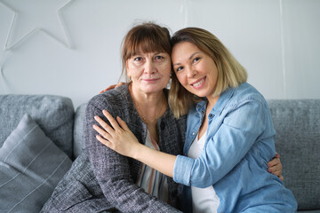 Head shot of beautiful adult daughter hug older mother at home, happy female two age generation family love