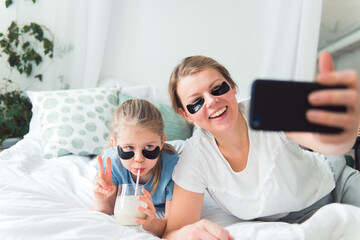 Mom and daughter using eye patches, drink smoothie and taking selfie or video call, spa and body...
