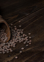 Foto vertical de un recorte de una cuchara para especias sobre una mesa de madera oscura y con lentejas esparcidas por la mesa.