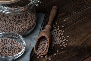horizontal picture with a glass jar with raw lentils on a rustic table next to a wooden spoon.