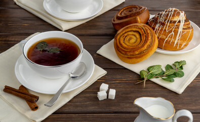 hot black tea in a white porcelain cup. selective focus. aromatic tea with sugar and mint. delicious cinnamon rolls for breakfast.