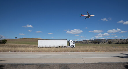 Truck on a freeway with plane flying overhead in Australian Country Town midway between Sydney and Melbourne with nice blue sky and lush green trees as a backdrop
