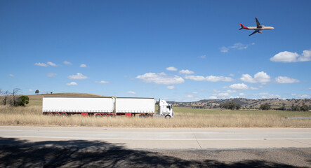 Truck on a freeway with plane flying overhead in Australian Country Town midway between Sydney and Melbourne with nice blue sky and lush green trees as a backdrop