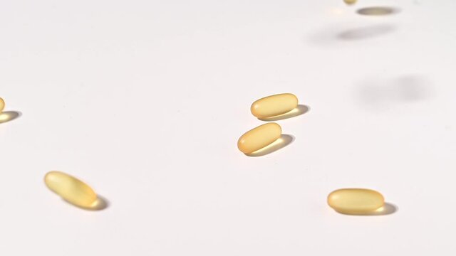 Close-up of falling transparent yellow capsules over white backdrop. Food supplements containing omega 3 and fish oil