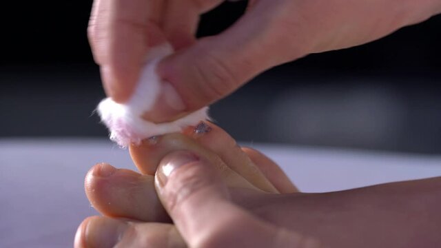 Woman removing a nail polish from her toes, sitting on the bed