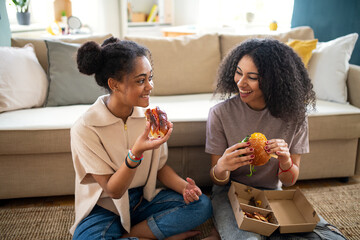 Portrait of young sisters indoors at home, eating burgers.