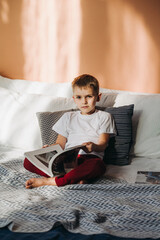A little boy is sitting on the bed leafing through a magazine