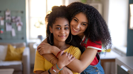 Portrait of young sisters indoors at home, looking at camera.