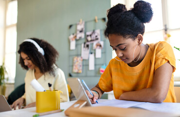 Portrait of young sisters with tablet indoors at home, e-learning concept.