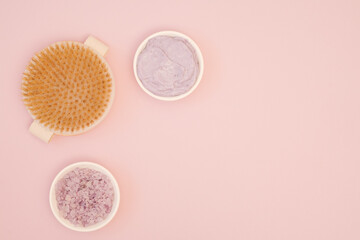 Home spa body care. Set of body cosmetics on pink background with copy space. Anti-cellulite massage brush, lavender sea salt, organic homemade body scrub. Flat lay, top view