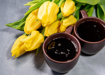Two cups of tea or coffee, yellow tulips on a gray background. Close-up