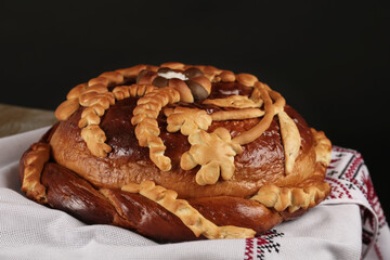 Rushnyk with korovai on table against black background, closeup. Ukrainian bread and salt welcoming tradition