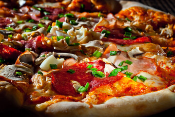 Pizza on a black table close up. Contrasting dramatic light as an artistic effect.