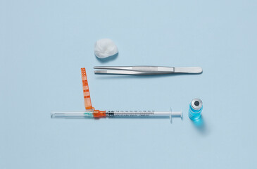 Vaccine syringe with medicine vial, tweezers and dressing on blue background