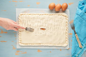 One person pricks the dough with a fork over the tuna, tomato, onion and bell pepper filling to...