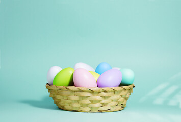 Easter background. A collection of Easter eggs in pastel colors in a basket on a blue-green background, with harsh shadows and light.