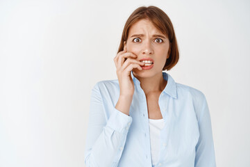 Portrait of scared and anxious young woman employee, biting fingers nails and looking worried, making small mistake, panicking, standing on white background