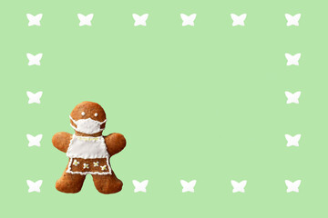 Cute gingerbread woman with protective face mask in a frame from butterflies, isolated, green background. Greeting card, copy space for text. Creative concept in coronavirus (COVID-19) time