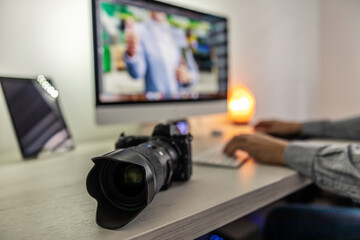 A photo zoom of the professional black camera on a neatly furnished desk. A man sits on a chair and...