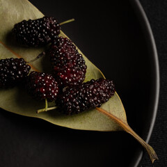 Black mulberries on green leaf and black dish