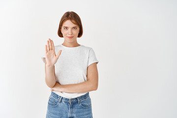 Confident smiling girl say no, showing stop palm gesture, prohibit action, standing on white...