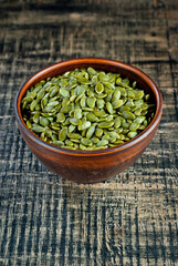 Peeled pumpkin seeds in a clay bowl on a wooden table. Seeds on a black shabby board. Copy space and free space for text near the seeds.