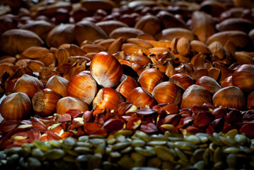 Many kinds of nuts close up. Heap of nuts on a black wooden board. Nuts are stacked on the table. Contrasting dramatic light as an artistic effect. Nuts in blue smoke.