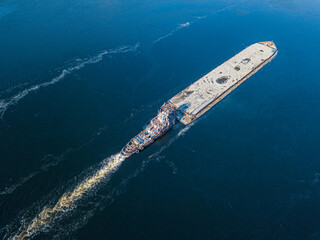 Obraz premium The barge floats on the freezing river. Aerial drone view. Sunny winter day, thin ice on the river.