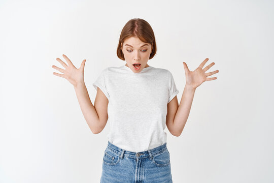 Surprised Woman Raising Hands Up, Gasping And Looking Down Wondered, Checking Out Advertisement, Amazing News, Standing Against White Background