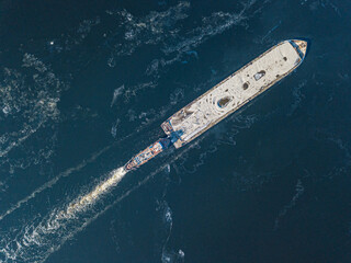 The barge floats on the freezing river. Aerial drone view. Sunny winter day, thin ice on the river.