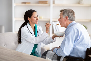 Obraz premium Medical assistance for elderly people with disabilities. Nurse feeding senior handicapped man in wheelchair at home