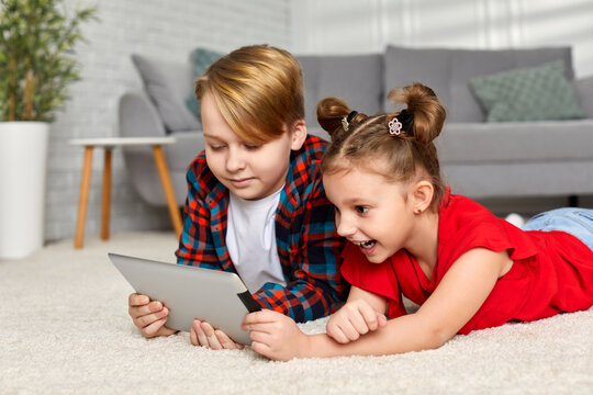 cute smiling brother and sister with tablet lying on carpet. Children use gadgets at home